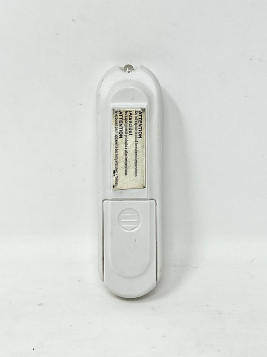 A white plastic handheld electronic device, shown from the back with a battery compartment cover open, revealing a battery and printed warning text.