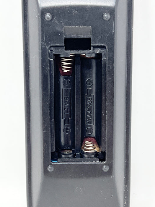 Close-up of a two-battery compartment in a dark gray plastic device, showing the battery terminals, spring contacts, and battery slots against a white background.