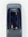 Close-up of a dark gray battery compartment cover with the cover removed, showing two 1.5V batteries installed in a dual-cell battery holder against a plain white background.