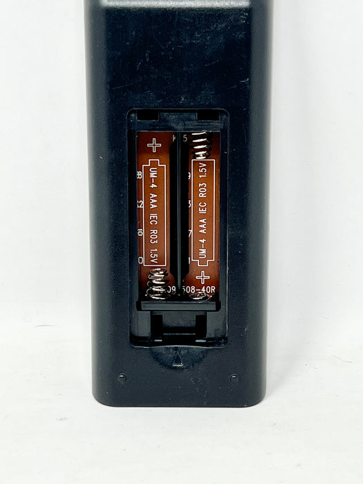 A close-up of a black plastic battery compartment cover with the back panel removed, showing two AA batteries installed inside. White printed text on the batteries reads 'UM-4 AAA IEC R03 1.