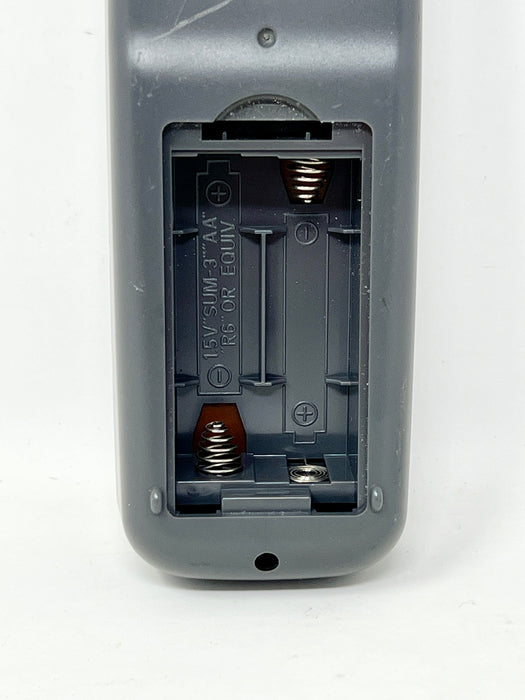Close-up of the back of a gray remote control showing the battery compartment with the cover removed, on a white background.