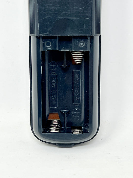 Close-up of the battery compartment of a black remote control, showing the internal springs and polarity markings on a white background.