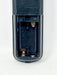Close-up of the battery compartment of a black remote control, showing the internal springs and polarity markings on a white background.