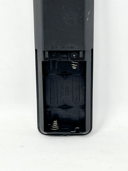 Close-up of the battery compartment of a black remote control, showing two batteries and metal spring contacts on a white background.