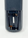 Close-up of the open battery compartment of a dark gray remote control, showing internal battery slots, springs, and contacts on a white background.