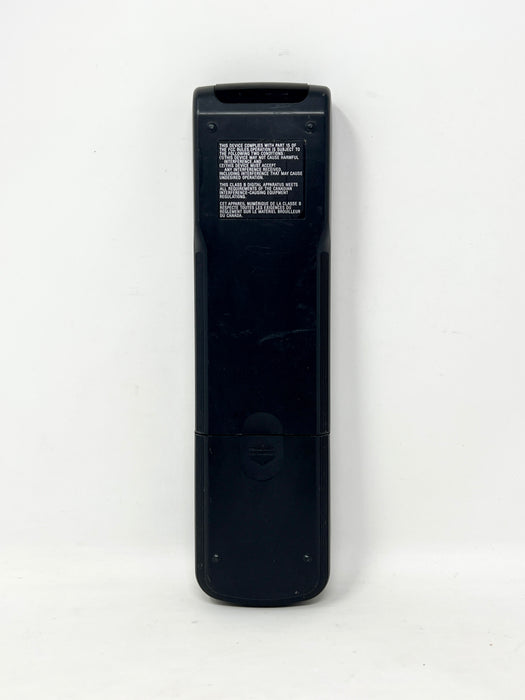 The back of a black plastic remote control with white printed text and a small circular button, shown vertically against a plain white background.