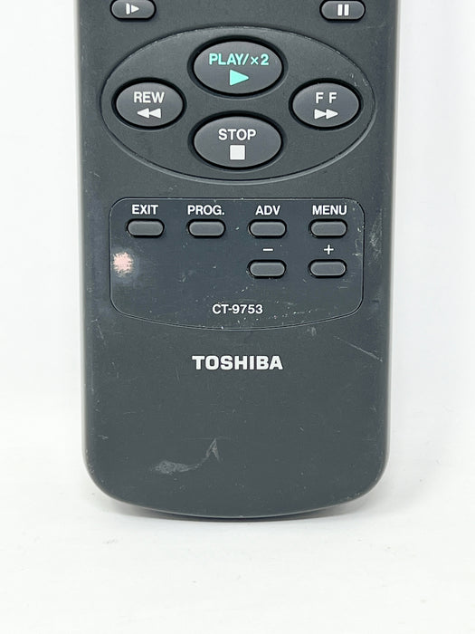 A close-up of a Toshiba remote control, model CT-9753, showing the front buttons including PLAY/x2,REW, STOP, FF, EXIT, MENU, and PROG.