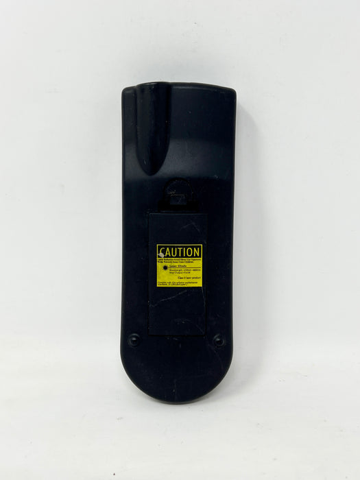 The back of a black plastic remote control with a yellow and black caution label, photographed against a plain white background.