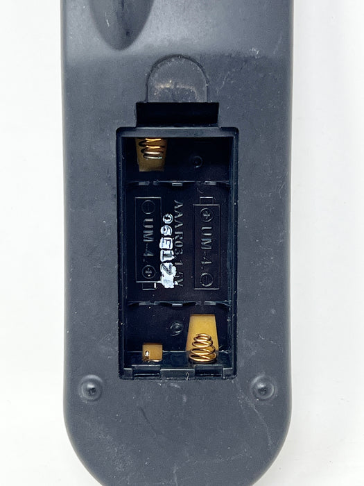 Close-up of the back of a black remote control showing the battery compartment with exposed gold-colored terminals and white battery contacts.
